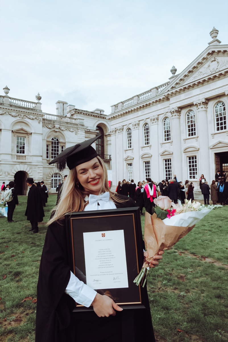 Graduation portrait holding a framed degree and flowers